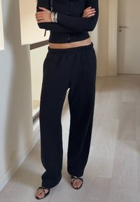 Pantalones deportivos sueltos negros con cintura elástica, confeccionados en material suave. Combinados con sandalias negras y un top corto acanalado.