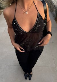 Črna zgornja majica na zaponke z odkritim materialom okrašena s srebrnimi kroglicami. Prilegajoče se črne hlače in črni čevlji z ostrimi konicami. Zlate nakitne poudarke.