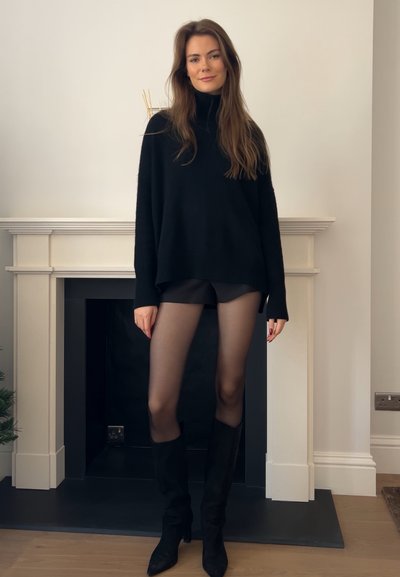 Suéter negro de gran tamaño con cuello alto, medias negras transparentes y botas negras hasta la rodilla. Textura suave, diseño relajado y silueta ajustada.