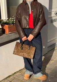 Personne portant une veste en cuir marron, un pull rouge, un jean large foncé retroussé en bas, des chaussures à plateforme couleur sable, et tenant un sac à main imprimé léopard.