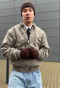 Γκρι bomber τζάκετ με φερμουάρ, ριμπ μανσέτες και λογότυπο στο στρίφωμα. Καφέ πλεκτό σκουφί και καφέ γάντια. Απαλές μπλε τζιν.