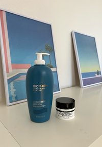 Biotherm Life Plankton body milk in een teal pompflacon naast de moisturizer van The Inkey List in een ronde zwarte pot, op een lichte ondergrond.