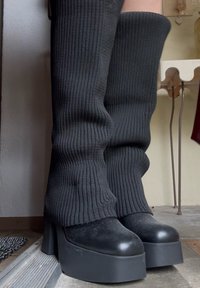 Črne teksturirane čizme do stegen z rebrasto tkanino in debelim podplatom, ki imajo gladek toe cap in brezšivno zasnovo.