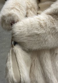 Witte nep bontjas met een zachte, pluizige textuur; heeft een leren riem met zilveren hardware. Close-up van de mouwdetails.