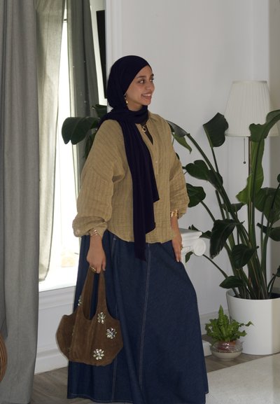 Blusa de manga larga texturizada en color beige, combinada con una falda de mezclilla oscura. Un bufanda oscura y un bolso marrón con adornos florales completan el atuendo.