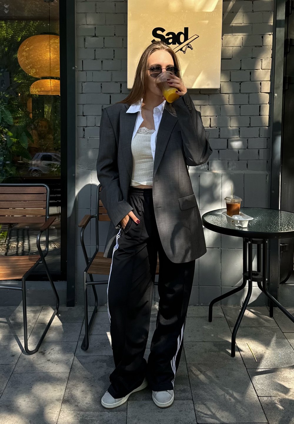 Blazer oversized cinza sobre um top cropped branco com rendas, combinado com calças de treino pretas com riscas brancas, e ténis brancos.