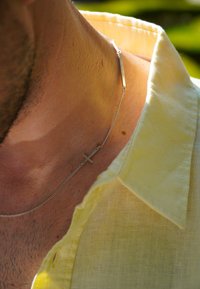 Hõbedane kettkaelakee ristripatsiga, kantud palja naha peal. Kandjal on seljas heledakollane lühikeste varrukatega särk.