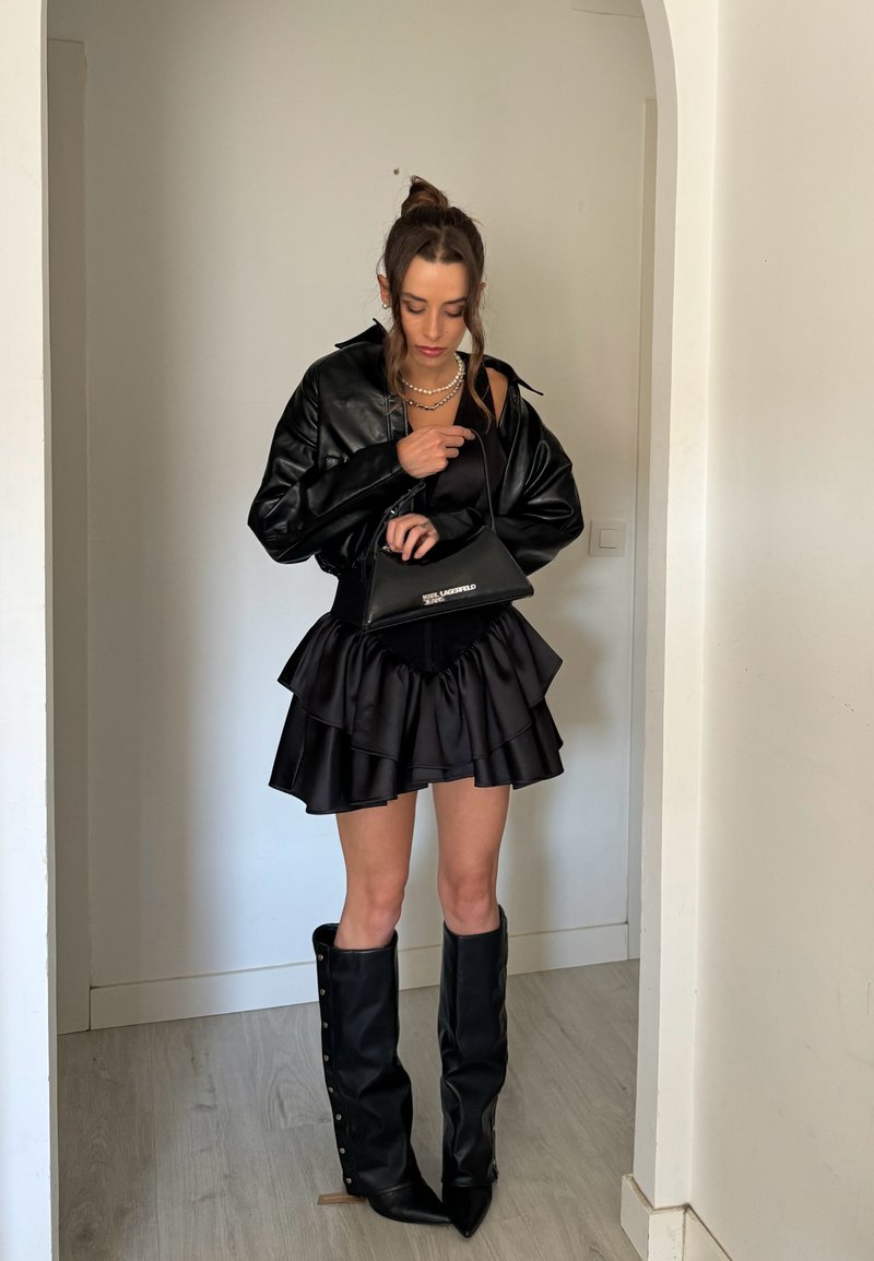 Fekete bőr cropped dzseki, rétegzett fekete mini szoknya, térd fölé érő fekete csizmák. Kiegészítve egy fekete táskával és gyöngy ékszerekkel.