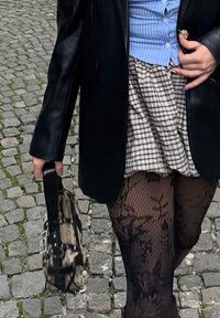 Fekete bőr blézer, kék csíkos ing, kockás szoknya, fekete csipkés harisnya és mintás kézitáska rövid füllel.