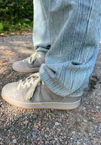 Sublinhados cinzentos em camurça com três riscas cinzentas mais escuras, atacadores de creme e solas de borracha bege, combinados com jeans de denim azul claro.