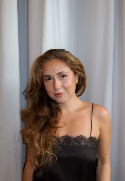 Camisón de seda negra con adornos de encaje, con tirantes finos de espagueti. El cabello es ondulado y el fondo tiene cortinas blancas. Luz sobre la piel.