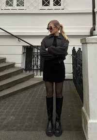Μαύρες μποτές μέχρι το γόνατο με πλατφόρμα, φόρεμα σε κολλητή γραμμή μαύρου χρώματος και γκρι υπερμεγέθη bomber τζάκετ. Γυαλιά ηλίου και μαλλιά σε αλογοουρά.