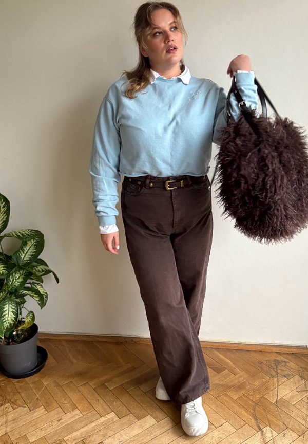 Šviesiai mėlynas ilgomis rankovėmis megztinis dėvimas virš baltos marškinių su apykakle, derinamas su tamsiai rudomis kelnėmis ir baltais sportbačiais. Išskirtinė rudų atspalvių tekstūruota rankinė papildo aprangą.