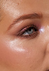 Nærbilde av et øye med glitrende rosa øyenskygge, definerte vipper og en fuktig, teksturert hudoverflate, med en lys rosa rouge.