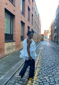 Fehér fodros felső fekete pöttyökkel, laza sötét farmerrel párosítva. Téglaházak és macskaköves utca városi környezetet biztosítanak.