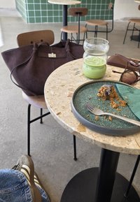 Barna vászontáska, kerek zöld tányér maradék tortával, villa, zöld ital üveg, mintás kerek faasztal, szürke betonpadló.