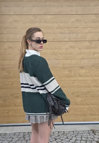 Grøn strikket cardigan med hvide og marineblå striber, båret over en hvid skjorte, parret med en ternet miniskirt og en lille sort taske.