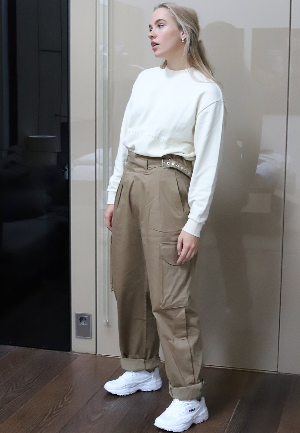 Beige Cargo-Hosen mit Oversized-Passform und Seitentaschen, kombiniert mit einem weißen Langarmshirt. Tragen mit weißen Sneakers. Glatte Textur.