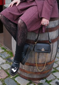 Mocassins noirs à franges avec un détail en imprimé vache blanc, associés à des collants noirs texturés et un petit sac noir avec une chaîne dorée et un logo.