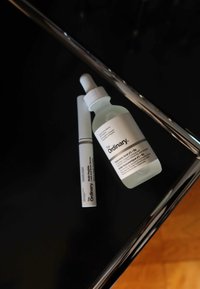 Klar glassflaske med hvit dråpeteller, merket «Hyaluronsyre 2 % + B5.» Slank hvit tube merket «Multi-Peptide Serum.» Begge på en mørk overflate.