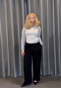 Haut gris clair à manches longues associé à un pantalon noir ample, posé devant un rideau gris. Tissu lisse avec une texture subtile.