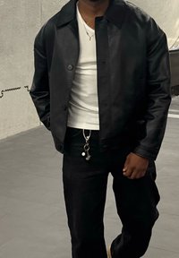 Must nahast jakk nööpidega, kantud valge soonikkoes särgi peal, koos mustade teksapükste ja dekoratiivse võtmehoidjaga.