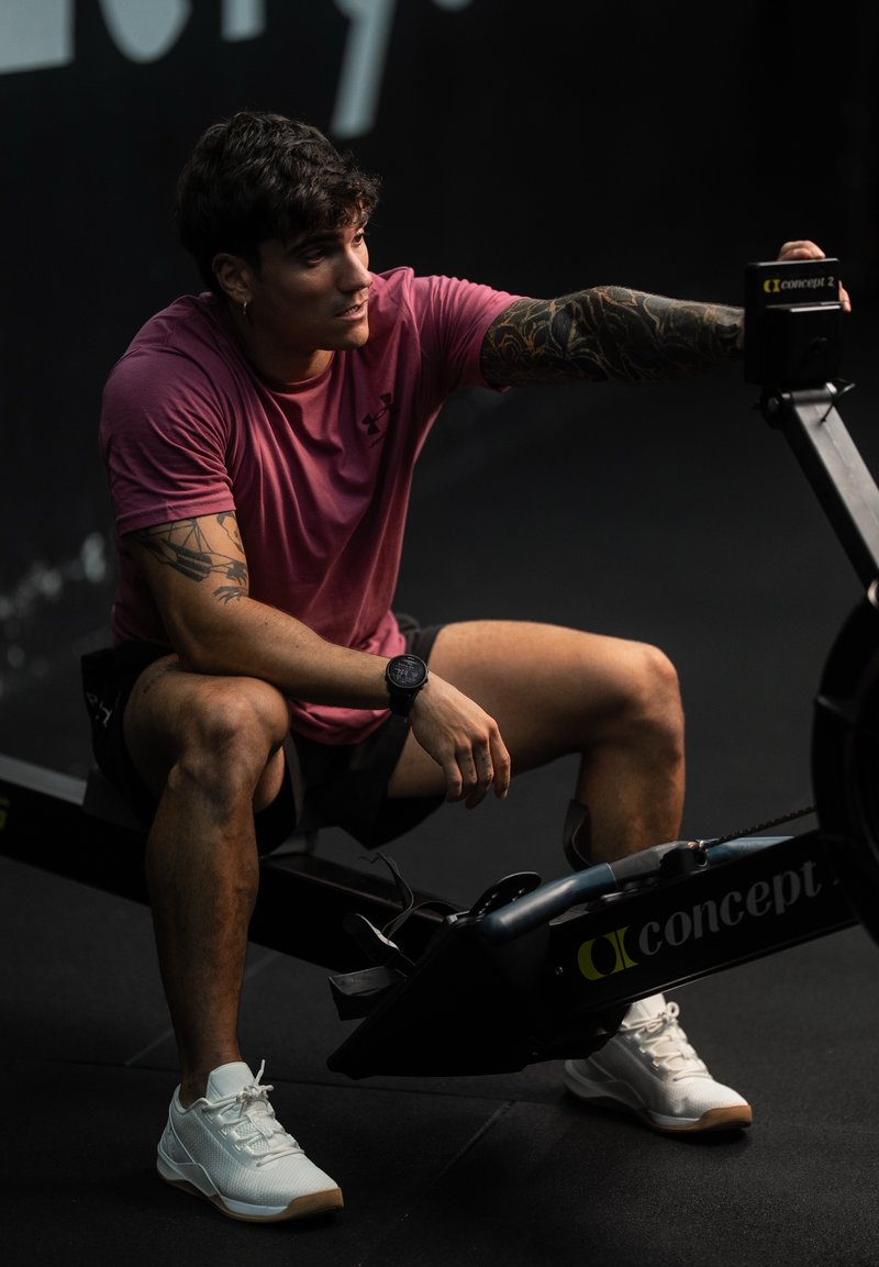 Concept2 romaskine med sort ramme. En person i en lyserød skjorte og shorts sidder på den, iført hvide sportsko og et ur.
