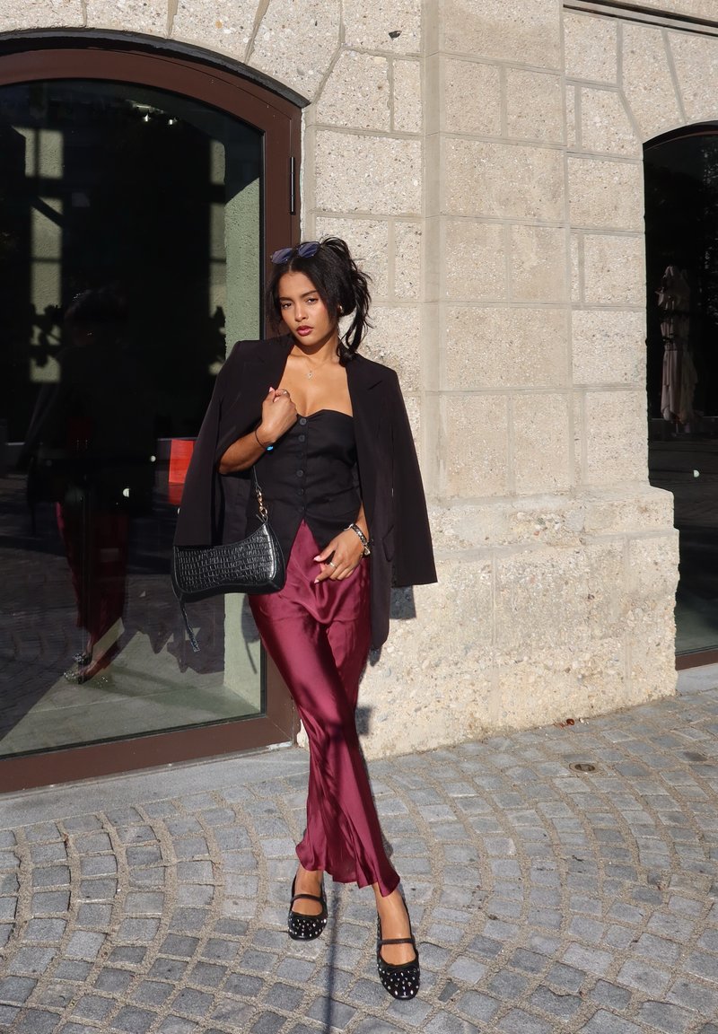 Μαύρη σακάκι πάνω από εφαρμοστό μαύρο τοπ, συνδυασμένο με γυαλιστερό μπορντό σατέν παντελόνι και μαύρα παπούτσια διακοσμημένα με καρφιά. Συμπεριλαμβάνεται τσάντα με υφή.