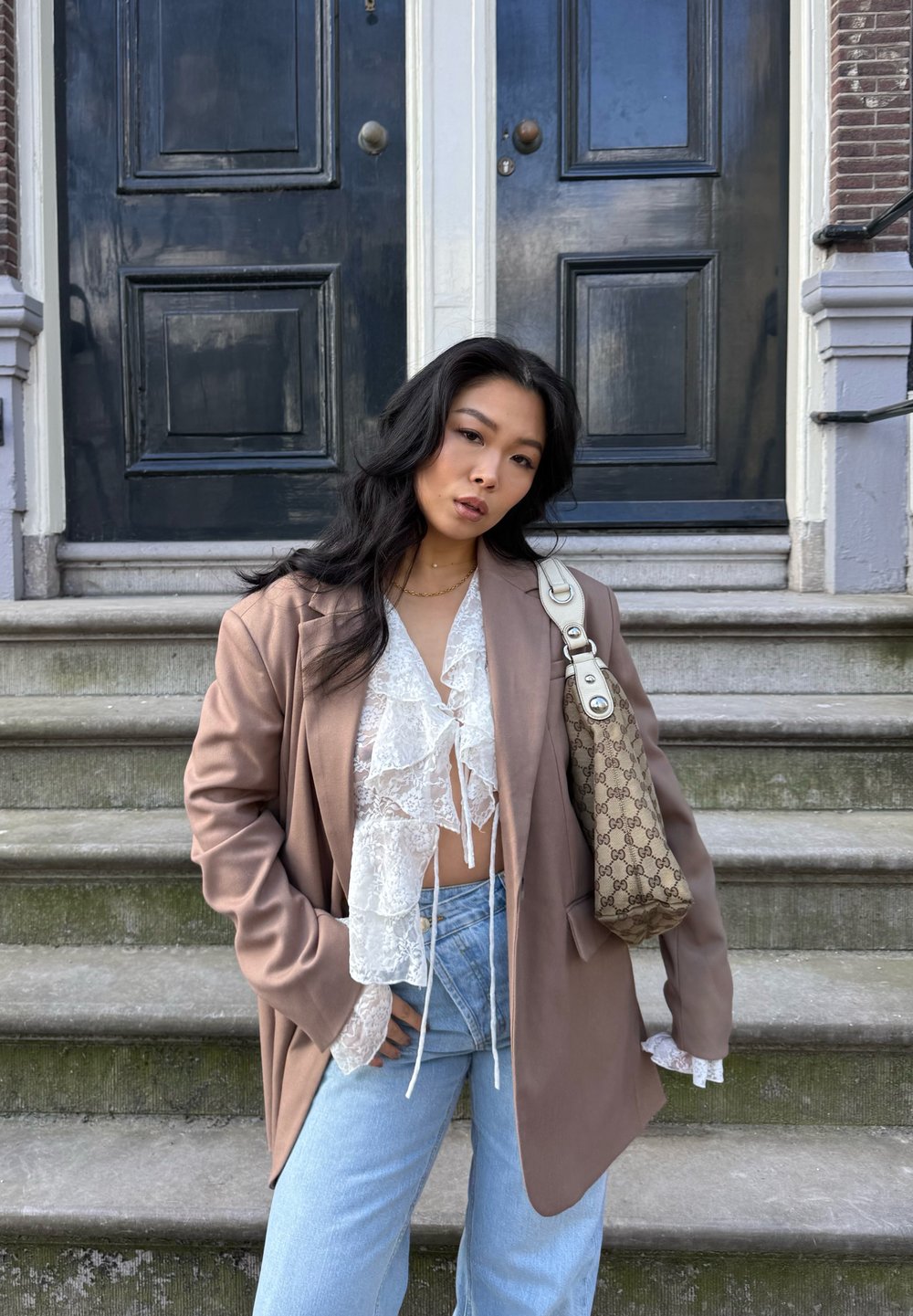 Brun oversized blazer over en hvid blondebluse med flæser, parret med lyseblå højtaljede jeans og en beige mønstret skuldertaske.