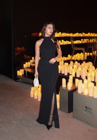 Robe noire à col licou avec une silhouette ajustée et une fente latérale, assortie à des talons noirs et un sac à main blanc, entourée de bougies jaunes.