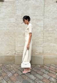 Vestito aderente di colore crema con maniche corte, bottoni centrali, abbinato a una borsa bianca con texture e sandali minimalisti con cinturini.