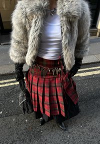 Műszőrméből készült szürke dzseki, fehér trikó, piros kockás, pliszírozott szoknya kulcstartós övvel, és fekete bőr kézitáska ezüst lánccal.