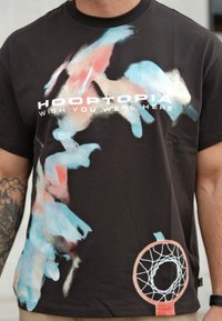 Czarny t-shirt z krótkim rękawem z abstrakcyjnym wzorem w odcieniach niebieskiego i różowego, z napisem "HOOPTOPIA ŻE PRZEKAZUJESZ" oraz grafiką obręczy do koszykówki.