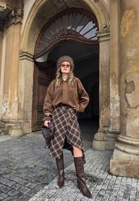 Pruun sametist üle suurusega särk õhupallivarrukatega, ruuduline seelik, pruunid põlve kõrgused saapad ja karvamüts, hoidmas pruuni käekotti.