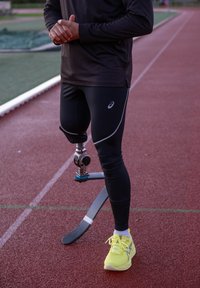 Schwarze Sportleggings mit silbernen Akzenten, eine mechanische Prothese mit einem gebogenen Kohlefaserfuß und leuchtend gelbe Laufschuhe.