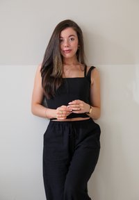 Zwart cropped top met vierkante halslijn, gecombineerd met zwarte drawstring broek. Gladde stof, minimalistisch ontwerp en subtiele gouden accessoires.