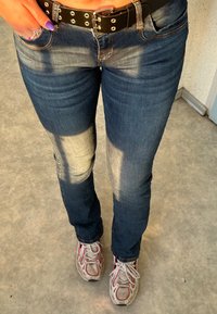 Mørkeblå denim jeans med let blegning ved knæene, parret med hvide og lyserøde sneakers samt et sort nitterbælte.