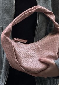 Bolsa de pele trançada rosa com uma alça curva e fecho em zíper, apresentando um padrão em cruz e uma textura suave.