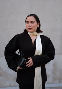 Blazer nero oversize con maniche a sbuffo, sciarpa crema annodata attorno al collo, borsa nera con accenti in argento, texture lisce, design minimalista.