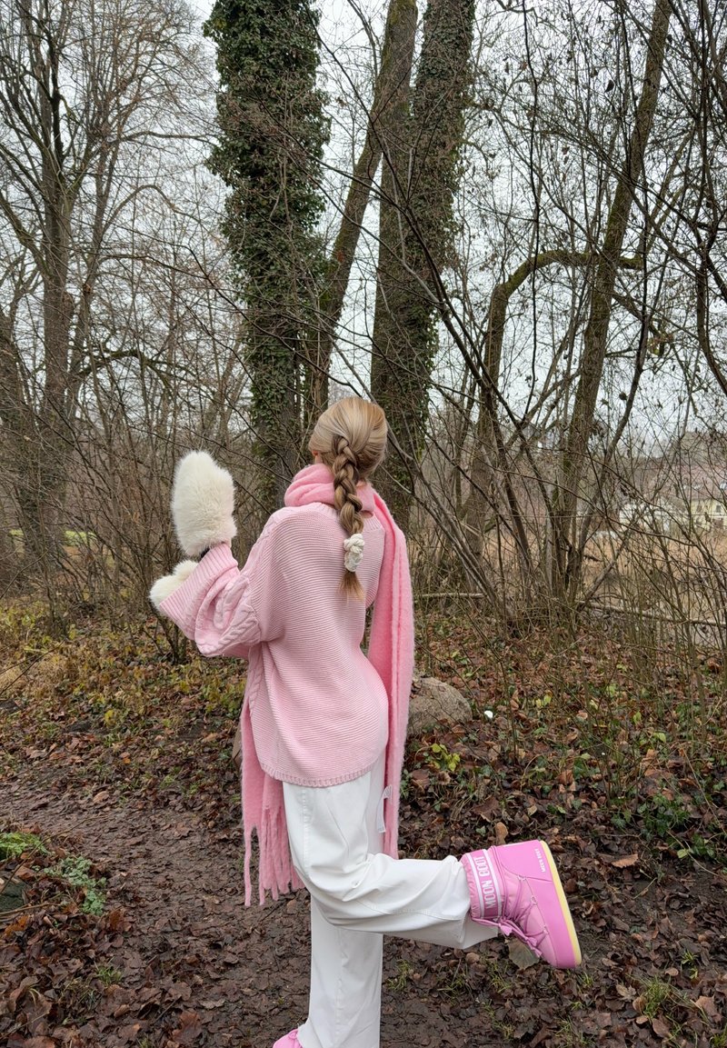 Pull rose surdimensionné à côtes, pantalon blanc, bottes roses et moufles blanches et duveteuses. Cheveux tressés et une écharpe rose complètent la tenue.