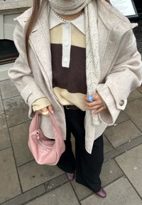 Ljusbeige ullkappa över en brun, creme och tan randig tröja. Svarta byxor, en rosa texturerad handväska och en stickad halsduk.