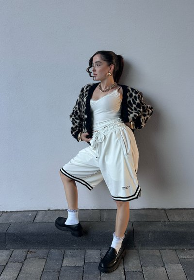 Pantalones cortos deportivos blancos con acentos de rayas negras, un cárdigan de estampado de leopardo negro y una blusa blanca ajustada con tirantes finos. Zapatos de plataforma negros.