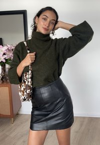 Zöld kötött garbó pulóver, fekete bőr miniszoknya és mintás válltáska barna részletekkel. Simább textúrák és laza szabás.