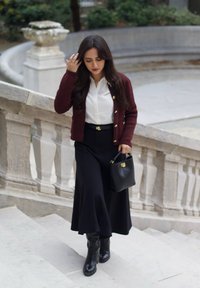 Maroon cardigan with gold buttons over a white blouse, black skirt with a flared hem, black leather knee-high boots, and a black handbag.