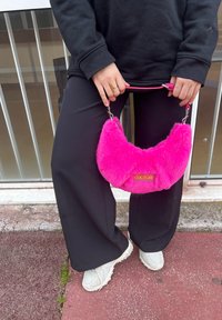 Τσάντα κατασκευασμένη από ψεύτικη γούνα σε έντονο ροζ χρώμα, σε σχήμα ημισελήνου, με χρυσό λογότυπο "COUTURE", συνδεδεμένη με ροζ λουρί και ασημένιες λεπτομέρειες.