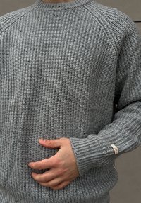 Sivý sveter z textúrovanej pleteniny s okrúhlym výstrihom a rebrovanými manžetami. Malá etiketa umiestnená na ľavej manžete.