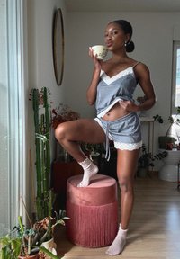 Grau pyjama-set mit Spitzenbesatz, bestehend aus einem Camisole und Shorts. Zubehör umfasst weiße Socken und eine florale Teetasse. Innenraum mit Pflanzen.