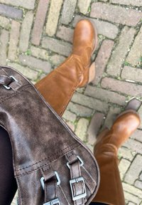 Bruine leren laarzen tot de knie met een ronde neus en een stevige hak, gecombineerd met een donkerbruine tas met zilveren hardwareaccenten.