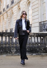 Black leather jacket over a white shirt, paired with a black skirt and ankle boots. Setting features classic architecture and stone balustrade.