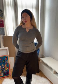Graues Langarm-Henley-Shirt mit Knopfleiste, kombiniert mit schwarzen Shorts. Das Outfit wird durch ein schwarzes Stirnband und kniehohe Stiefel erg�änzt.